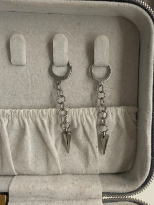 Silvriga örhängen  - Säljer ett par silvriga örhängen i metall med cool kedjedesign och spetsig kon längst ner. Örhängena har en modern och edgy vibe, perfekta för att lyfta din stil. Passar dig som gillar detaljer och vill sticka ut lite extra. Dem är egengjorda i rostfritt stål. 