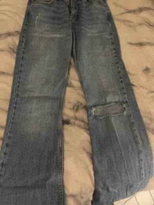 Blå raka jeans med ett hål - Säljer ett par blå raka jeans från gina i storlek 34. Jeansen har ett hål på ena benet. ny pris 599.