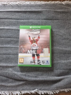 NHL 16 till Xbox One - NHL 16 är ett ishockeyspel från EA Sports till Xbox One. Omslaget är grönt med en spelare i röd matchtröja som lyfter Stanley Cup-pokalen. Spelet har SHL och NHL-licenser och rekommenderas från 12 år.