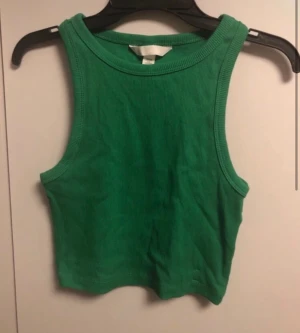 Grön ribbad linnetopp från H&M - Snygg grön ribbad linnetopp från H&M i storlek XS. Toppen är croppad och har breda axelband samt rund halsringning. Perfekt för varma dagar eller som layering-piece till din outfit.