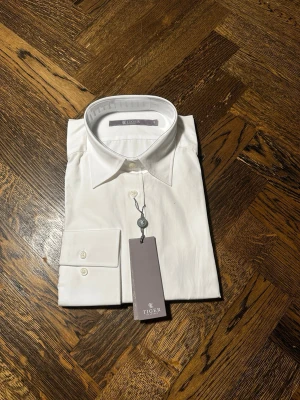 Vit skjorta från Tiger of Sweden - Klassisk vit skjorta från Tiger of Sweden Skjortan har en stilren design med krage och är tillverkad i bomull i storlek 44 alltså L/XL