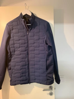 Mörkblå vindjacka från Adidas strl S - Snygg mörkblå vindjacka från Adidas med quiltad framsida och släta ärmar. Jackan har dragkedja framtill och står upp i kragen. Perfekt för blåsiga dagar och enkel att matcha med olika outfits.
