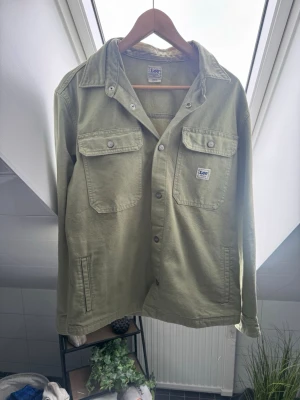  overshirt från Lee - Olivgrön overshirt från Lee med två bröstfickor med lock och knapp, samt sidofickor. Klassisk krage och knappstängning framtill. Tillverkad i ett mjukt bomullstyg som ger en avslappnad look. Perfekt lager på lager-plagg för en casual stil. Nytt skick, använd få gånger. Säljs för att den inte passar pris kan diskuteras. Ny pris 1200kr