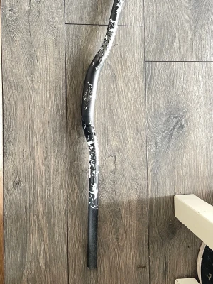 Svart böjd cykelstyre och funkar på alla G2  - Säljer ett svart cykelstyre med böjd form och vita detaljer. Styret är tillverkat i metall och har ett unikt mönster på ena sidan. Perfekt för dig som vill ge din cykel en personlig touch.
