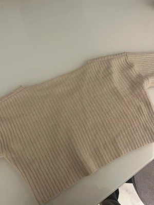Beige ribbstickad tröja med V-ringning - Säljer en beige ribbstickad tröja med V-ringad hals. Tröjan har långa ärmar och är gjord i ett mjukt, stretchigt material som känns skönt mot huden. Perfekt för dig som gillar en enkel men stilren look.