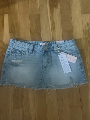 Ljusblå jeanskjol med slitningar - Trendig ljusblå jeanskjol med slitna detaljer och rå kant nertill. Kjolen har aldrig andvänts likadan kjol från spegel bilden men inte samma. Kjolen är från Gina Tricot 