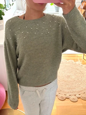 Grön stickad tröja med pärlor - Jättefin grön stickad tröja från H&M med fina vita pärlor över bröstet och axlarna. Den är använd och är lite nopprig, men annars är den i ett bra skick. Kontakta om du har frågor💕