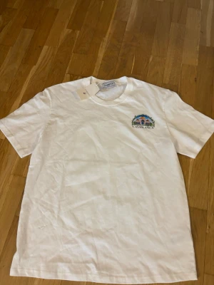 Vit t-shirt från Casablanca - Säljer en vit t-shirt från Casablanca med ett färgglatt broderat motiv och logga på bröstet. Klassisk rund hals och korta ärmar. Perfekt för dig som gillar stilrena plagg med en twist.