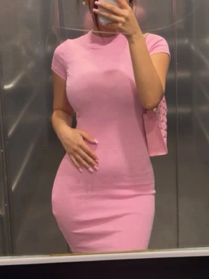 Rosa tight kortklänning - Säljer en rosa tight kortklänning med korta ärmar och rund hals. Klänningen har en enkel, stilren design och är figurnära i passformen. Perfekt för dig som gillar en feminin och trendig look.