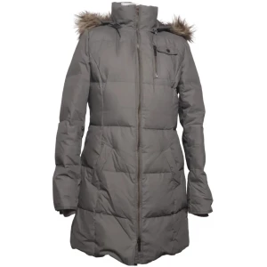 Grå lång dunjacka med fuskpäls - Säljer en grå lång dunjacka med huva och fuskpälsdetalj. Jackan har dragkedja framtill, bröstficka med dragkedja och quiltad design. Perfekt för kalla vinterdagar och håller dig varm och snygg.