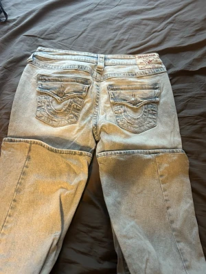 Ljusblå True Religion jeans - Säljer ett par ljusblå jeans från True Religion med klassiska kontrastsömmar och snygga fickdetaljer bak. Dem är uppsydda så dem passar mig perfekt som är 166cm. Har aldrig använt dem för jag inte är bekväm i lågmidjat. Köpte dem i umeå för 1300kr