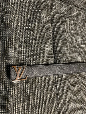 Svart  monogram skärp - Snyggt svart skärp  med klassiskt monogrammönster och logga i metall som spänne. Perfekt accessoar för att lyfta din outfit med en exklusiv touch. Skärpet har en stilren och tidlös design.