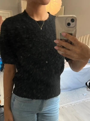 Svart stickad kortärmad topp - En enkel och stilren svart stickad topp med korta ärmar och rund hals. Perfekt att matcha med jeans eller kjol för en clean look. Materialet känns mjukt och bekvämt mot huden.