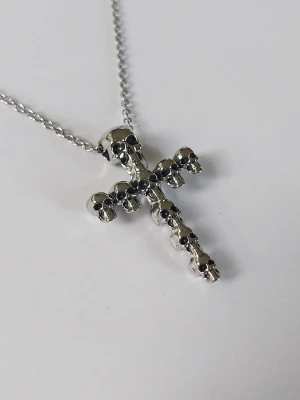 halsband med dödskallekors skullcross  - halsband med ett korsformat hänge dekorerat med små dödskallar. Kedjan är tunn och smidig, och hänget har en cool, edgy vibe som sticker ut. Materialet rostfritt stål 