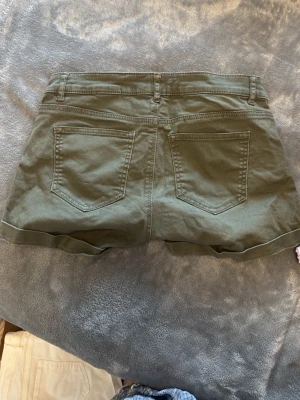 Olivgröna shorts från H&M - Snygga olivgröna shorts från H&M med klassisk femficksdesign och uppvikta benslut. Tillverkade i bomull med dragkedja och knapp framtill. Pris kan diskuteras 