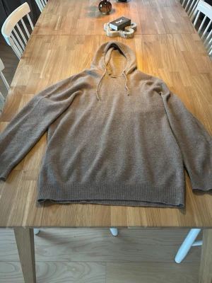 Beige Kashmir hoodie - Mysig beige stickad hoodie med huva och dragsko. Tröjan har ribbade muddar vid ärmslut och nederkant, samt en avslappnad passform. Perfekt för dig som gillar en enkel och stilren look. Materialet känns mjukt och skönt mot huden.