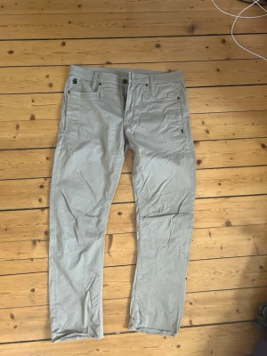 Beige chinos med raka ben - Snygga beige chinos med raka ben och klassisk passform. Byxorna har fem fickor, bälteshällor och stängs med knapp och dragkedja. Tillverkade i ett mjukt bomullsmaterial som är skönt att bära. Perfekta för en clean och avslappnad stil.