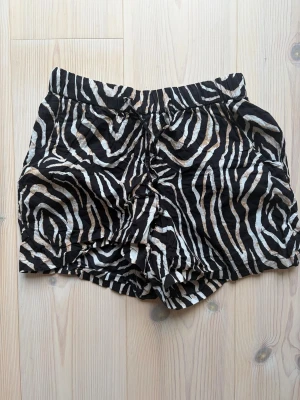 Zebramönstrade shorts med snörning - Snygga shorts med zebramönster i svart, vitt och beige. De har en avslappnad passform och snörning i midjan för extra komfort. Perfekta för varma dagar när du vill sticka ut lite extra.