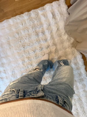 Ljusblå slitna baggy jeans xs - Säljer ett par ljusblå baggy jeans med flera slitningar och hål på benen. Jeansen har låg midja, raka ben och klassiska fem fickor. Perfekta för en avslappnad och trendig look. Från Gina 