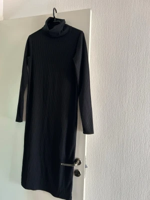 Svart ribbad långklänning polo - Säljer en svart långklänning med polokrage och långa ärmar. Klänningen är ribbad och har en rak passform som ger en stilren look. Perfekt för dig som gillar minimalistisk stil och vill ha något bekvämt men ändå snyggt.