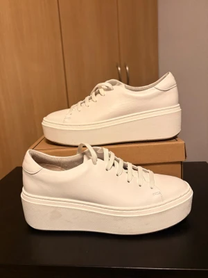 Vita platåsneakers med tjock sula - Snygga vita sneakers med rejäl platåsula och klassisk låg design. Skorna har vita snören och är tillverkade i slätt material som ger en clean look. Perfekta för dig som vill ha extra höjd och en stilren vibe till outfiten. Sneakers från märket Tamaris