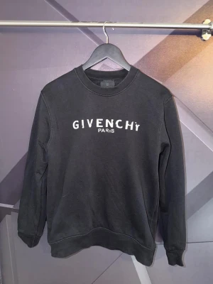Givenchy tröja - Svart sweatshirt från Givenchy med vit logotyptext på bröstet. Klassisk rund halsringning och långa ärmar. Tillverkad i mjukt material som känns skönt mot huden. Perfekt för en avslappnad och trendig look.
