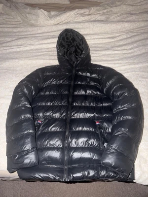 Svart dunjacka med huva från Polo Ralph Lauren - Säljer en svart dunjacka från Polo Ralph Lauren med huva och dragkedja framtill. Jackan har två fickor med dragkedja och diskret broderad logga på bröstet. Perfekt för kalla vinterdagar och riktigt skön att bära.
