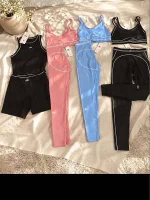 Alo sportset i svart, rosa och blå - Säljer flera snygga sportset från Alo. Ett svart set med linne och cykelbyxor, ett rosa set med sport-bh och tights samt ett blått set med sport-bh och tights. Alla har vita kontrastsömmar och är gjorda i stretchigt funktionsmaterial.