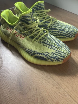 Yeezy Boost 350 V2 Semi Frozen Yellow - Säljer ett par Yeezy Boost 350 V2 Semi Frozen Yellow med stickad ovandel i gul och blå zebramönstrad Primeknit, gula snören och sula i gummi med brun detalj framtill. Sidan har röd SPLY-350 text. Riktigt unika sneakers för dig som vill sticka ut. Som trendade för några år sedan. Aldrig använd