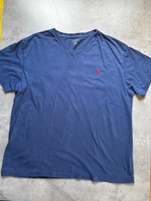 Marinblå V-ringad t-shirt Polo Ralph Lauren - Snygg marinblå t-shirt från Polo Ralph Lauren med V-ringning och klassisk röd broderad logga på bröstet. Tillverkad i mjuk bomull som känns skön mot huden. Perfekt för en avslappnad och stilren look.