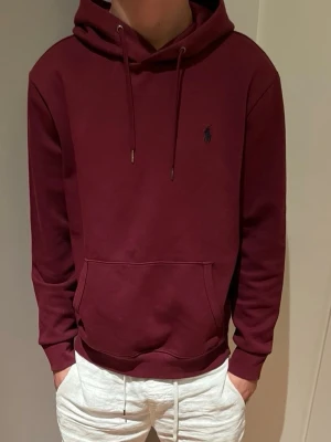 Unik Vinröd Ralph lauren hoodie - Säljer en unik vinröd hoodie med huva och dragsnören. Klassisk känguruficka framtill och diskret broderad logga på bröstet. Hoodien har ribbade muddar vid ärmslut och nederkant. Riktigt skönt material som passar nästan alla årstider.