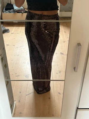 Brun paljettkjol med rak passform - Säljer en lång, brun kjol täckt med glittrande paljetter. Kjolen har en rak passform och hög midja, vilket ger en snygg siluett. Materialet är stretchigt och skimrar i ljuset, perfekt för att sticka ut. Supersnygg att styla med en enkel topp.