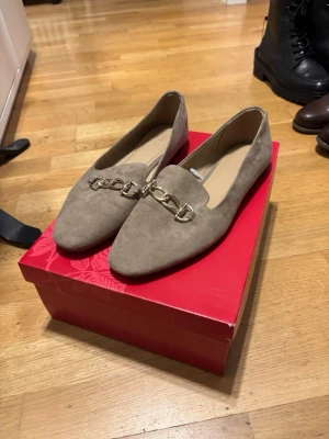Beige loafers med guldkedja H&M - Snygga beige loafers i mockaimitation med dekorativ guldfärgad kedjedetalj framtill. Skorna har en klassisk, spetsig tå och låg klack. Perfekta för dig som vill ha en stilren och trendig look. vid frågor eller om ni vill ha fler bilder är det bara att höra av sig!