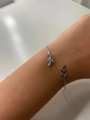 Silvrigt armband med blad - Snyggt armband i silverfärgad metall med öppet avslut och dekorativa blad på båda ändarna. Armbandet går att justera beroende på hur du vill att de ska sitta och hur din arm är formad
