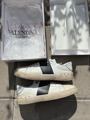 Valentino Garavani vita och svarta sneakers letar Byte! - Snygga sneakers från Valentino Garavani i vitt läder med en bred svart detalj på sidan. Skorna har lågt skaft och en chunky sula med nitar runt hälen för en cool touch. Perfekta för dig som vill ha en stilren men ändå unik look. Letar byte!