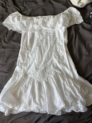 Vit offshoulder klänning Gina Tricot - Söt vit offshoulder klänning från Gina Tricot med broderade spetsdetaljer och volangkant. Klänningen har en romantisk känsla med sitt luftiga tyg och fina hålmönster. Perfekt för varma dagar och somriga tillfällen.