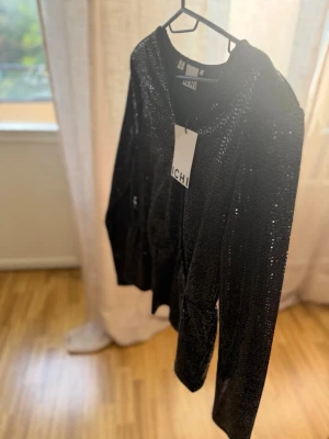 Svart glittrig topp från ICHI - Säljer en svart långärmad topp från ICHI täckt med glittriga paljetter. Perfekt för dig som vill sticka ut med en snygg och trendig look. Toppen har rund halsringning och en figurnära passform.