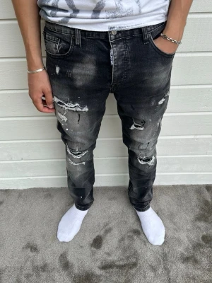 Svart/grå jeans helt nya - Hej, helt nya svart/mörkgråa jeans med slitningar och paintsplatter. Modellen på bilden är 183cm och väger 68kg. Liknande dsq2 jeans fast till ett väldigt billigt pris. Fick som gåva men var inte min stil. Storlek 32/32. Hör av dig vid andra frågor eller funderingar. Mvh