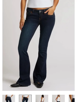 Mörkblå bootcut jeans med kontrastsömmar - Snygga mörkblå bootcut jeans med kontrastsömmar och klassiska fem fickor. Jeansen har låg midja och detaljerade bakfickor med lock och knapp. Tillverkade i stretchig denim för skön passform. Mörkblåa true religion jeans i modellen low waist joey. Storleken i byxorna äe w26, de är uppsydda så innerbenslängden är 74 cm. Lite slitningar längst ner vid fötterna. Pris kan diskuteras 