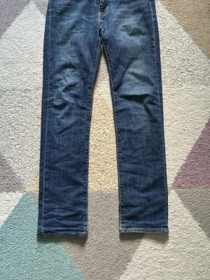 Levis Straight Bootcut Jeans - Klassiska blå jeans med rak passform och fem fickor. Jeansen har snygga slitningar och kontrastsömmar, samt detaljer i kopparfärg vid fickorna. Tillverkade i denim med en autentisk tvättad look. Perfekta för en avslappnad och stilren outfit.