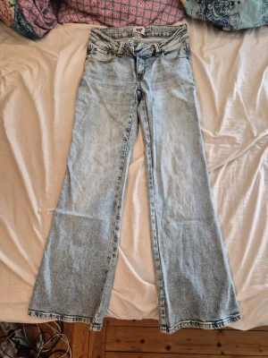 Ljusblå lowrised bootcut jeans med brodyr - Säljer ett par ljusblå bootcut jeans med snygg brodyr på bakfickorna. Jeansen har klassisk femficksmodell, låg midja och vida ben. Perfekta för dig som gillar retrostil och vill ha ett par jeans som sticker ut lite extra.