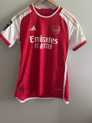 Arsenal matchtröja röd/vit - Snygg Arsenal matchtröja från Adidas i rött och vitt med guldiga detaljer. Köpt från Arsenals egna hemsida för ungefär 1200kr och har knappt använts!🤗