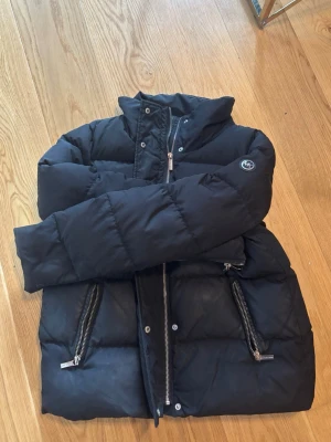 Michael kors pufferjacka  - Michael kors jacka, 2500 nypris om inte mer. Snygg svart pufferjacka med hög krage och två framfickor med silverfärgade dragkedjor. Jackan har quiltad design och en patch på ena ärmen. Perfekt för kalla vinterdagar och riktigt skön att bära. Väldigt varm och bära alltså!