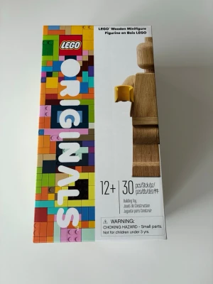 LEGO Originals Wooden - Unik LEGO Originals minifigur i trä, ca 20 cm hög. Figurerna har klassisk LEGO-design med rörliga armar och gula plastdetaljer. Förpackningen innehåller 30 delar och är färgglad med LEGO-mönster. Perfekt för samlare eller som dekoration.