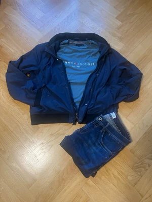 Komplett Märkesoutfit – Gant & Tommy Hilfiger - snygga och matchande märkesoutfiten som ett färdigt paket. Allt är i jättebra skick!  Mörkblå lättviktsjacka (Gant) (Nypris över 2000 kr). Storlek L   Blå/grå t-shirt (Tommy Hilfiger) storlek L   Mörkblå jeans (Hilfiger Denim) storlek 32/32  Tveka inte att fråga något. Obs! Inga förhandlingar 
