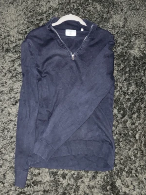 Mörkblå stickad tröja med halvzip - Mörkblå stickad tröja med halv dragkedja i halsen. Tröjan har långa ärmar, ribbade muddar och en klassisk passform. Perfekt för lager på lager och enkel att matcha med olika outfits.