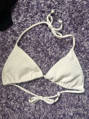 Vit trekantsbikini med knyt - Säljer en stilren vit trekantsbikini med knyt i nacken och ryggen. Bikinin har en lätt strukturerad yta och pärlor i ändarna på snörena💗
