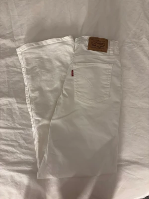 Vita wide leg jeans från Levi's - Säljer ett par vita jeans från Levi's med rak passform och klassisk femficksdesign. Jeansen har medelhög midja, silverfärgade nitar och Levi's ikoniska läderpatch bak. Perfekta för en clean och fräsch look året runt. Jeansen är i storlek 140cm!💕