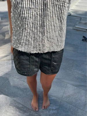 Svarta shorts i skinn med broderi - Snygga svarta shorts i skinn med broderade detaljer och blommigt mönster. De har en normal passform och är perfekta för sommaren. Ger en cool och trendig vibe till din outfit.