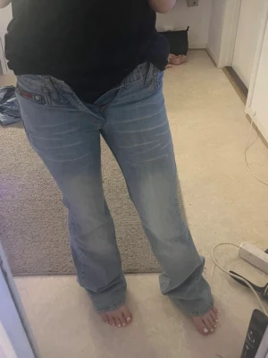 Ljusblå bootcut jeans - Säljer ett par ljusblå bootcut jeans med klassisk femficksdesign och låg midja. Jeansen har en avslappnad passform och är tillverkade i mjuk bomull. Perfekta för en chill och trendig look.